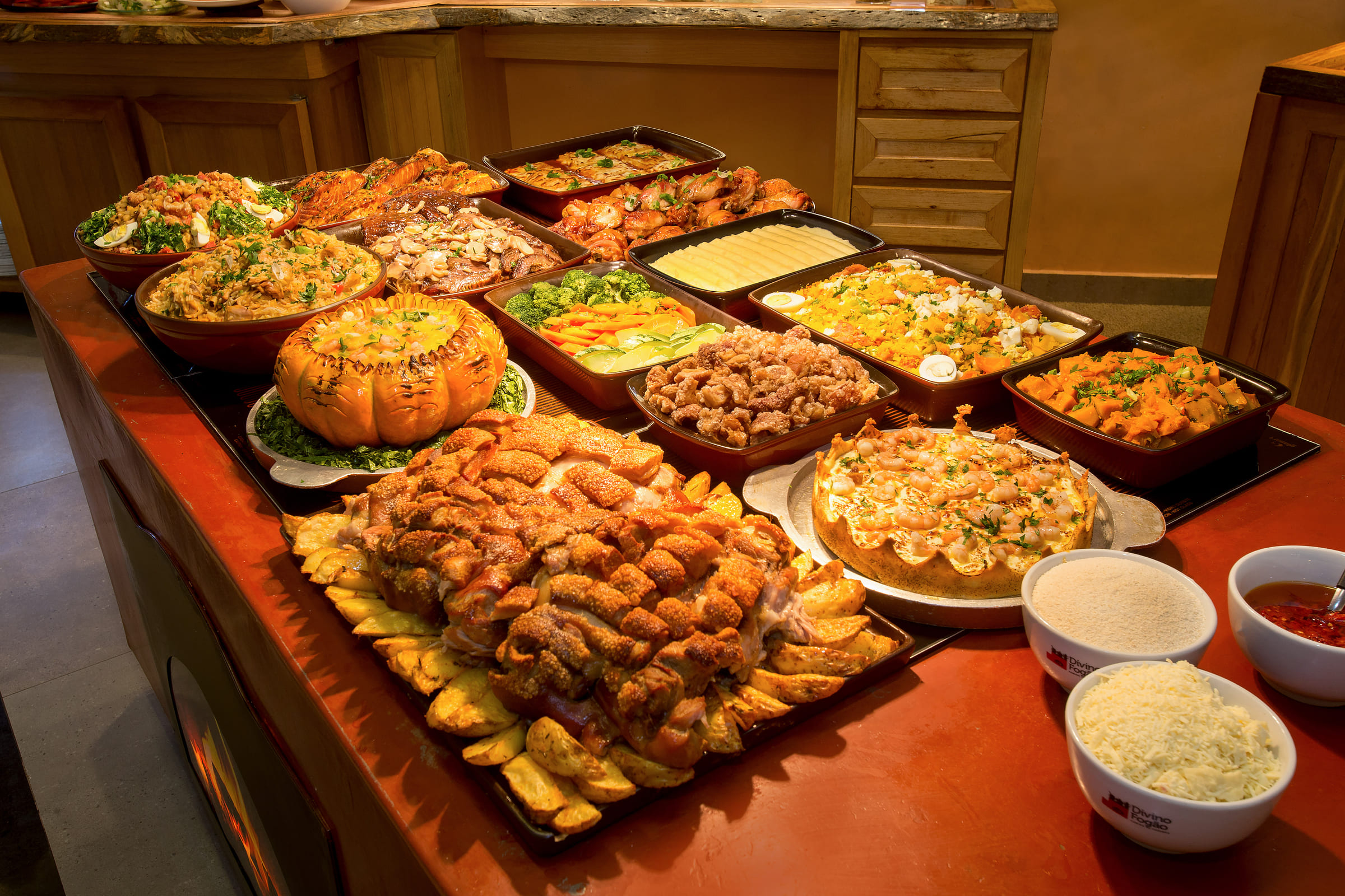 Linha do bufê Divino Fogão com travessas de carnes, arroz, farofa, legumes e acompanhamentos